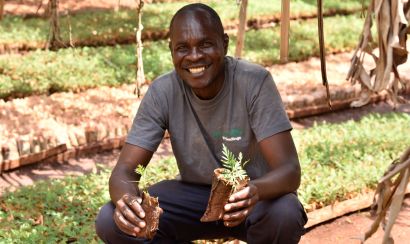 A smiling smallholder farming holding two tree seedlings 